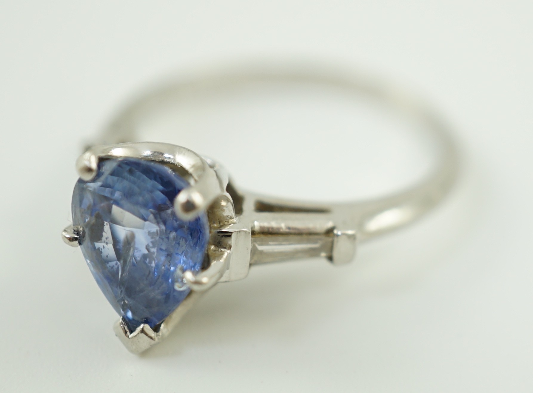A platinum (10%) and single stone pear cut Ceylon sapphire set ring, with tapered baguette cut diamond set shoulders